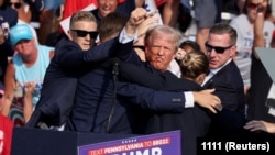 13-июль, 2024-жыл. Пенсильвания, Батлер. Трампты жансакчылары окуя болгон жерден алып чыгып баратышат.
