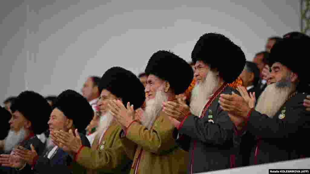 Аксакалы — мужчины-старейшины — аплодируют, наблюдая за празднеством с трибуны. И Бердымухамедов-старший, и его предшественник Сапармурат Ниязов построили культы личности, которые включают тщательно продуманные подношения и памятники