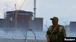 Військовослужбовець із російським прапором на формі стоїть біля Запорізької АЕС